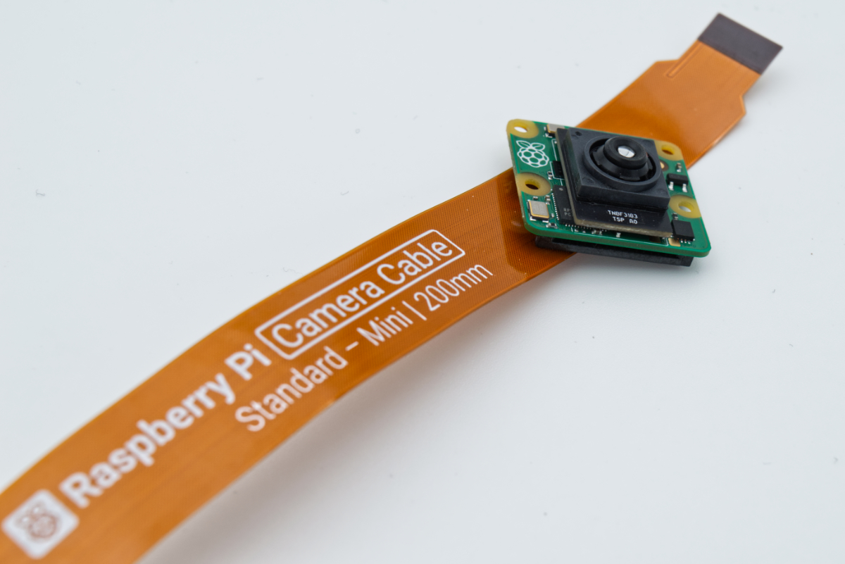 A close-up photo showing the Raspberry Pi AI Camera sitting against a camera ribbon cable.