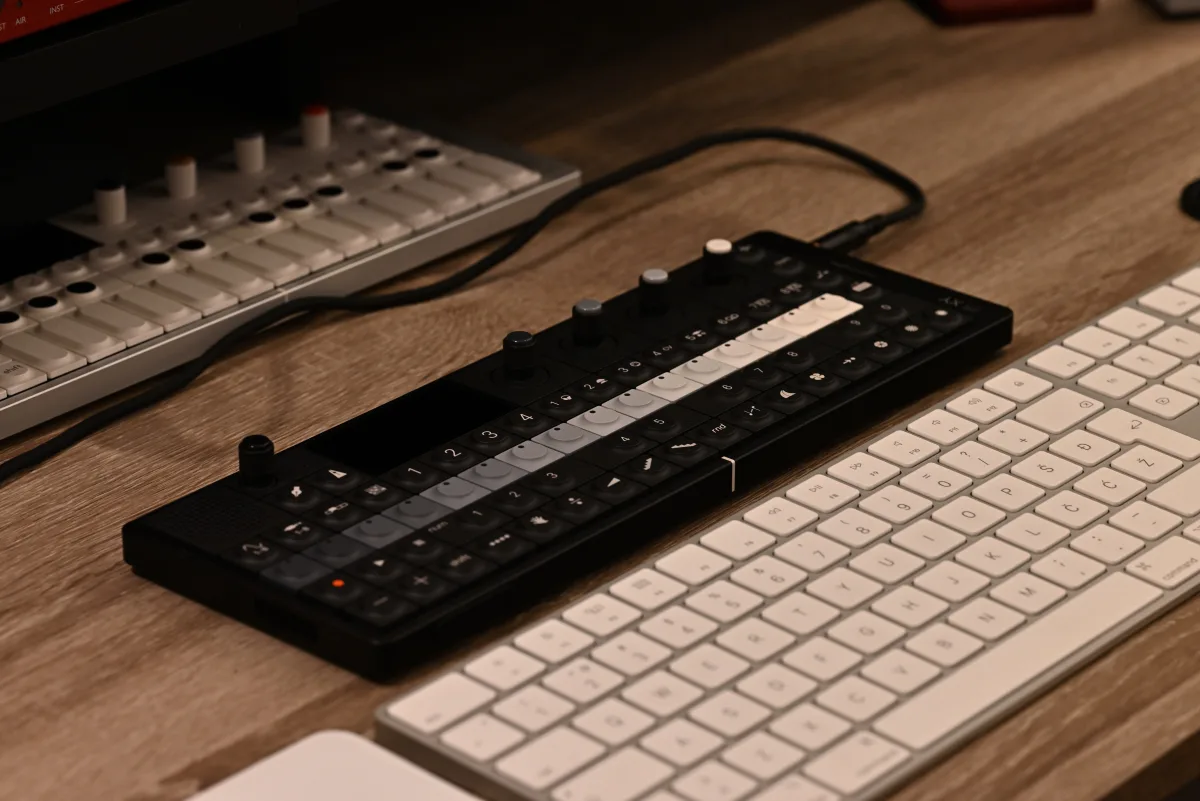 A photo of the OP-XY in between an OP-1 field and an Apple Magic Keyboard, showing its compact footprint.