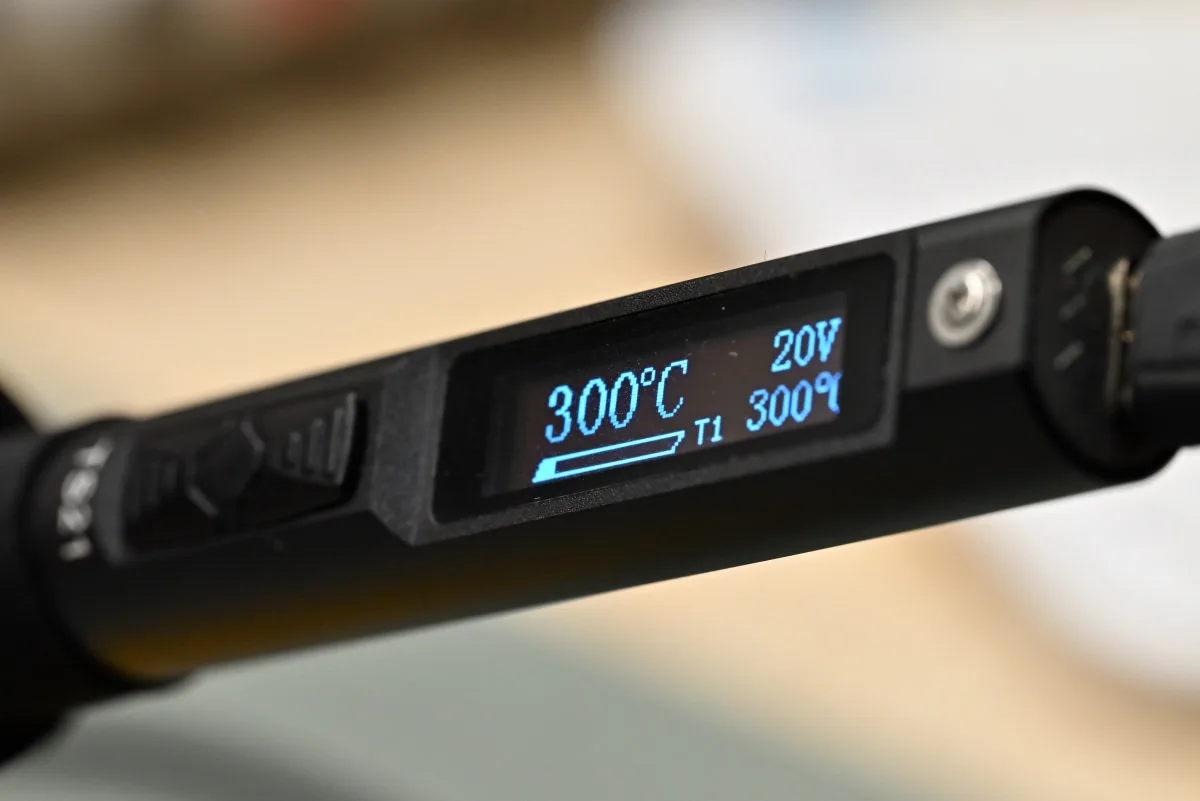 A photo of the screen interface during heating mode, showing multiple interface elements: most prominently the current temperature; followed by, in counter-clockwise order, current power, temperature preset setting and voltage.