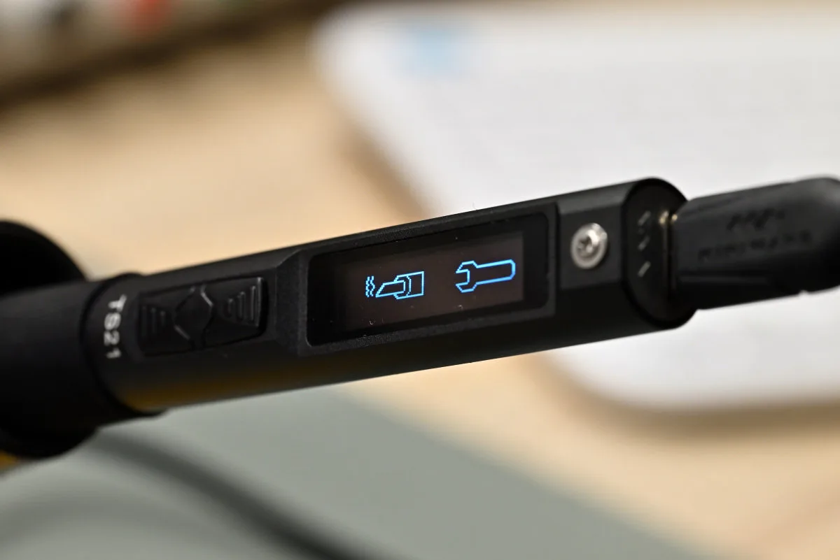 A photo showing the TS21 in standby mode, showing the screen graphics. On the screen's left is a symbol of the iron's tip emitting heat, used to access heating mode, while the wrench icon on the right symbolizes settings.