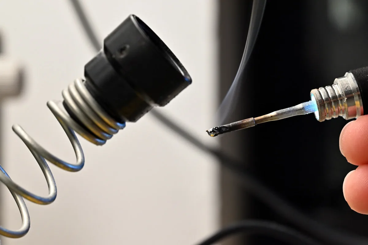 A photo showing the TS21 in use, with its LED ring light turned on, illuminating a puff of smoke from the solder flux being burned.