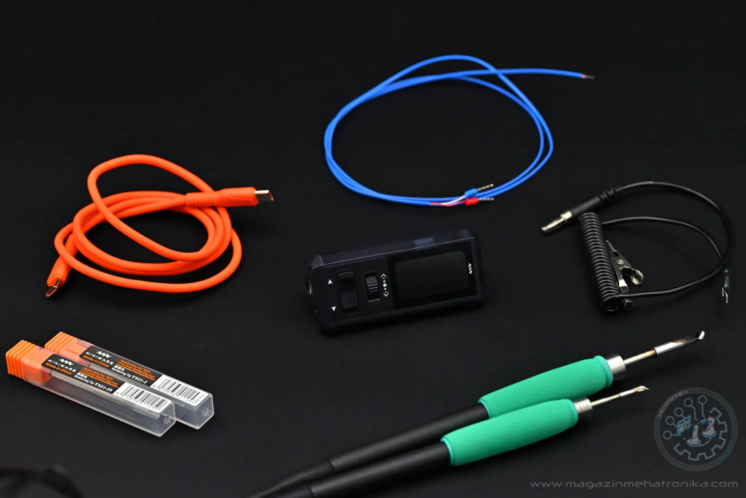 A photo of the Miniware TS1M together with all of the accessories we've tested: two extra cartridges, a USB cable, the thermocouple, the station itself, the sleep wire and two soldering handles.