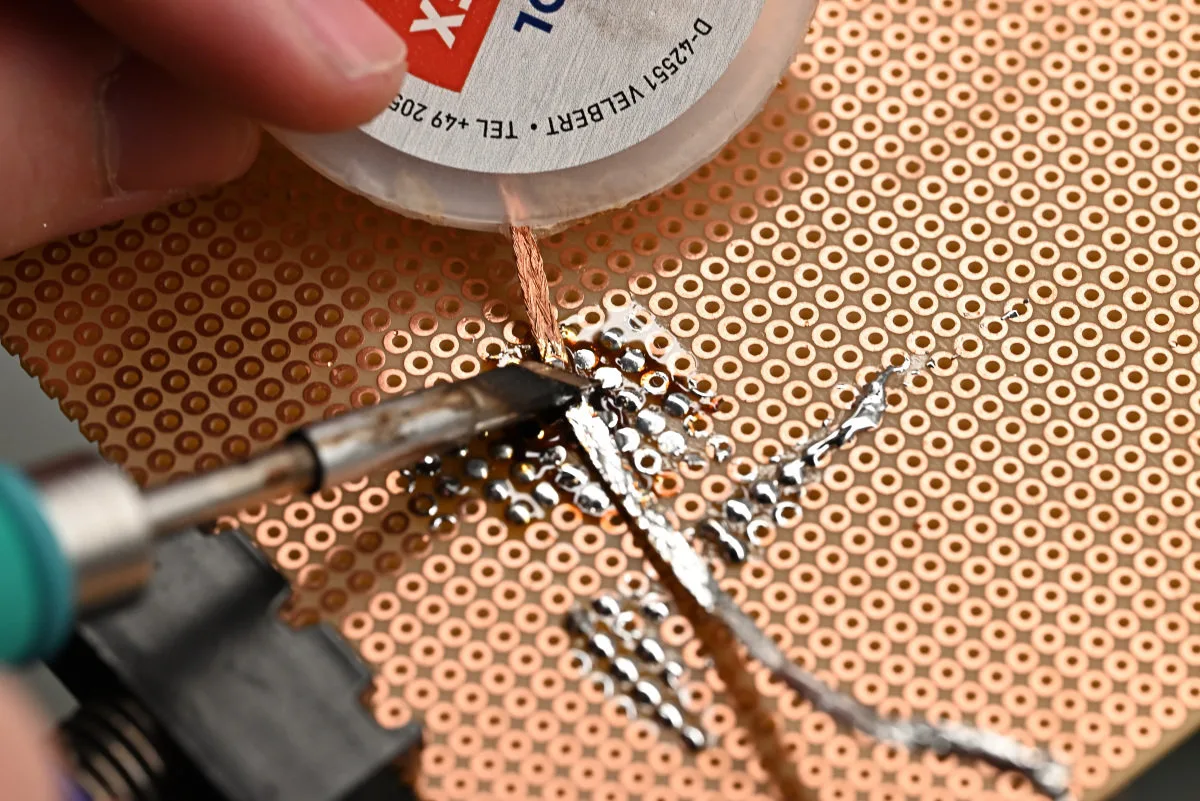 A photo that shows the C245 knife tip being used to heat a bit of copper wick, removing a large amount of solder.