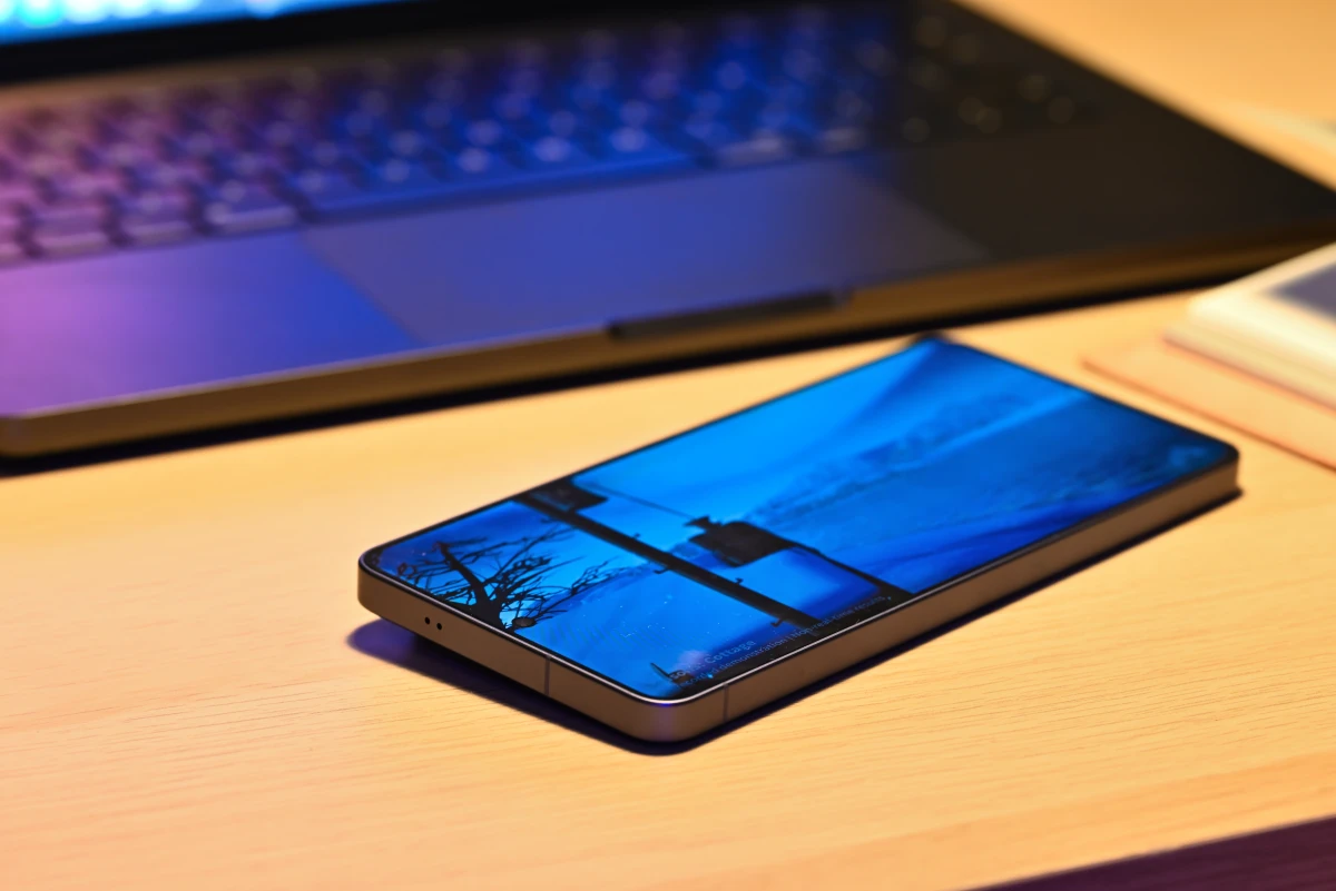 A photo of the S26 Ultra running one of the AnTuTu GPU tests, while resting on a table in front of a MacBook Pro and next to a notebook.